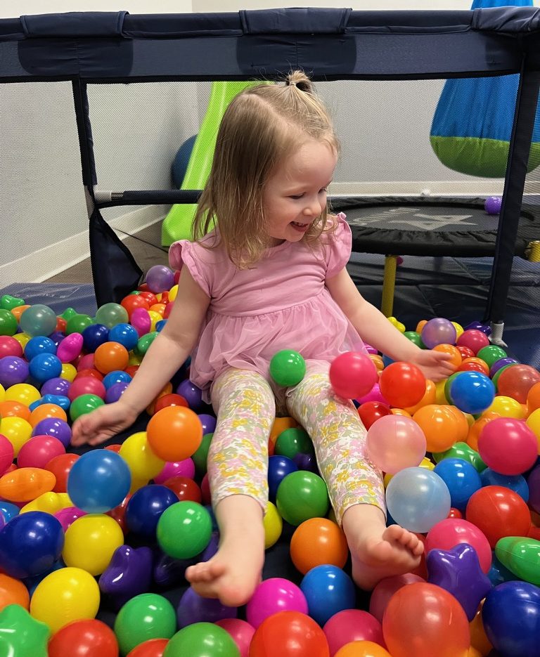 Child playing in colorful ball pit, smiling.