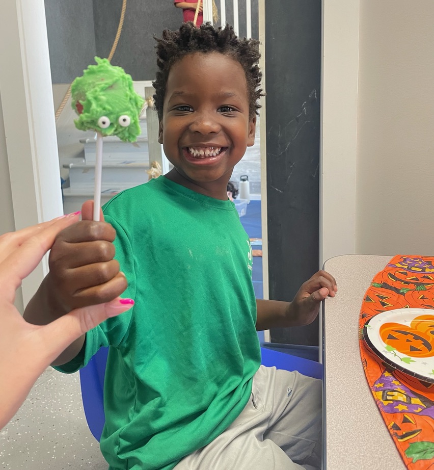 Child smiling with green monster cake pop.