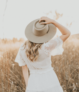 Woman in field wearing hat and white dress.