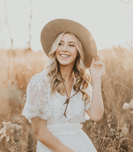 Woman in field wearing hat, smiling warmly.