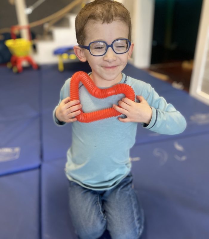 Child holding red toy heart, smiling indoors.
