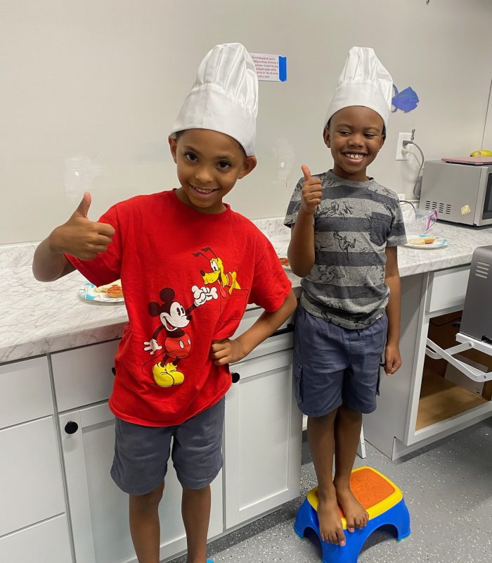 Two children in chef hats, smiling thumbs up.