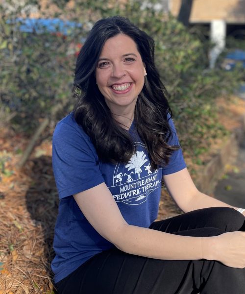 Smiling woman sitting outdoors on grass.