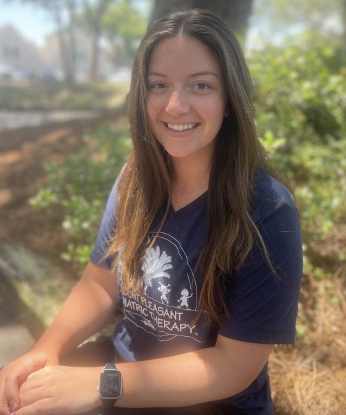Smiling woman sitting outdoors wearing a t-shirt.