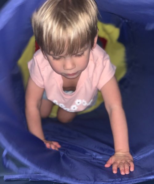 Child crawling through a colorful play tunnel.