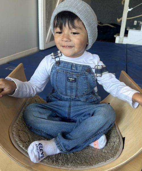 Child smiling, wearing overalls and a beanie.