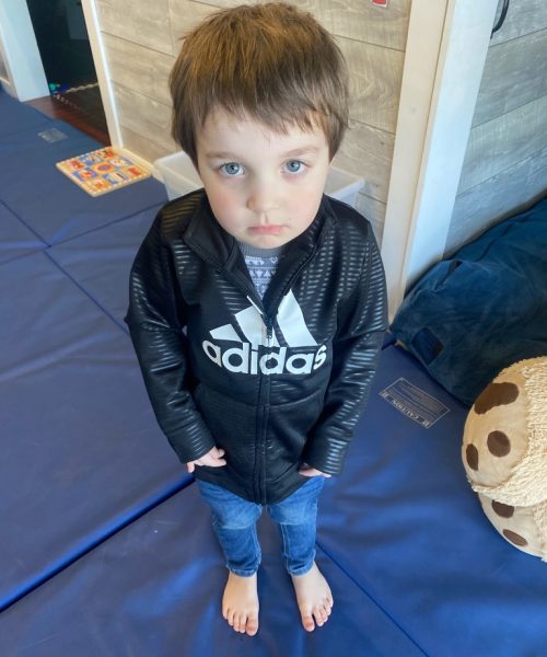 Young boy in black jacket, barefoot indoors.