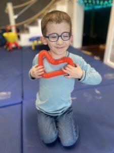Child holding red heart-shaped toy, smiling.