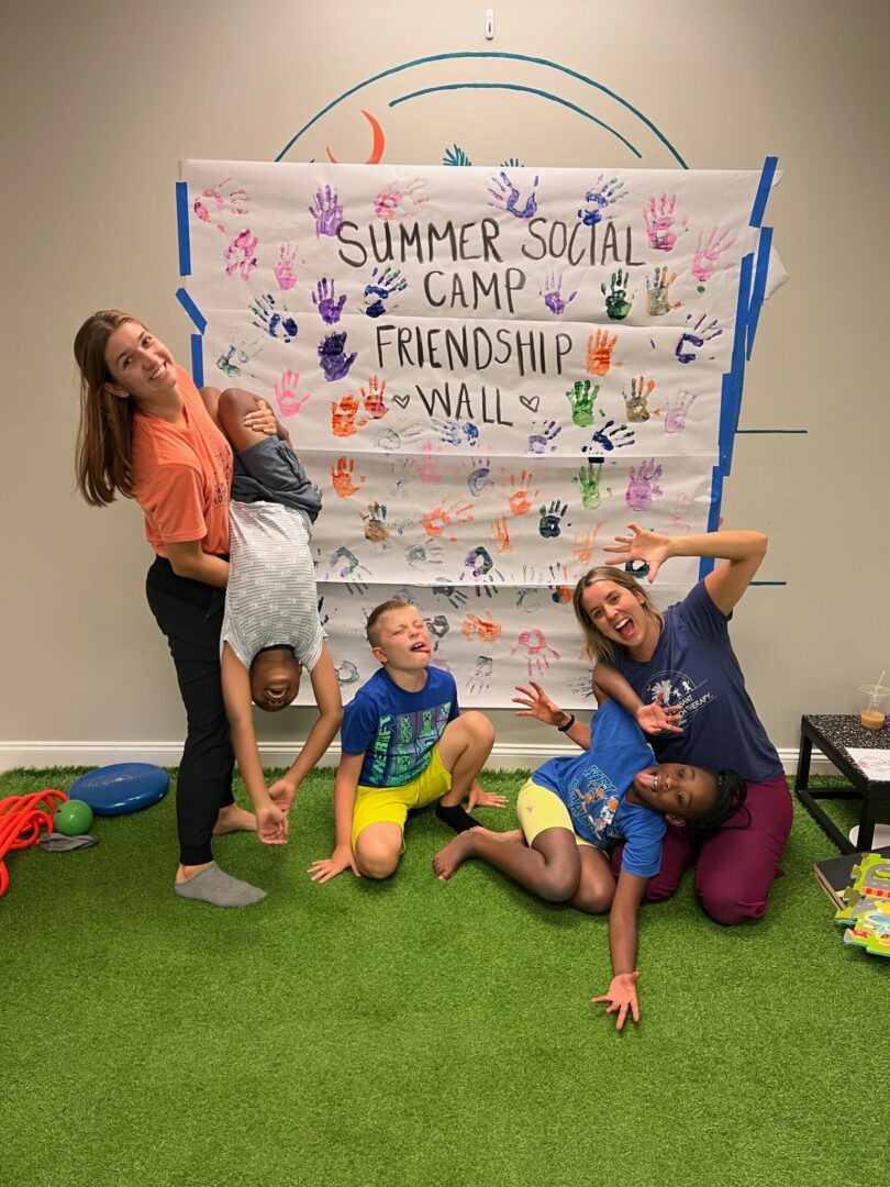 Four people posing cheerfully in front of a colorful summer camp banner.