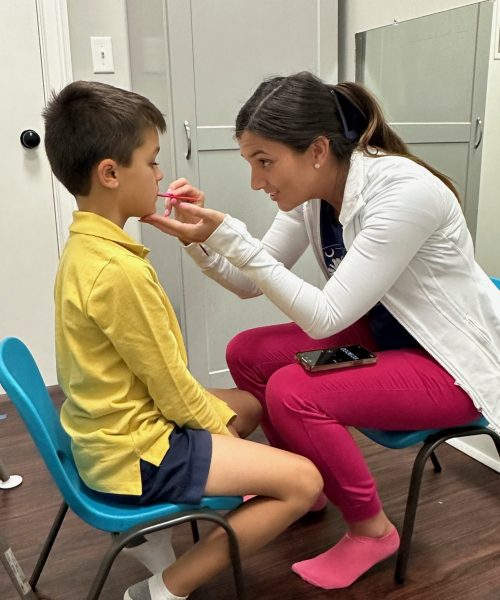 Woman examining boy's mouth in clinic setting.