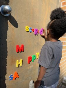 Child arranging colorful magnetic letters on door.