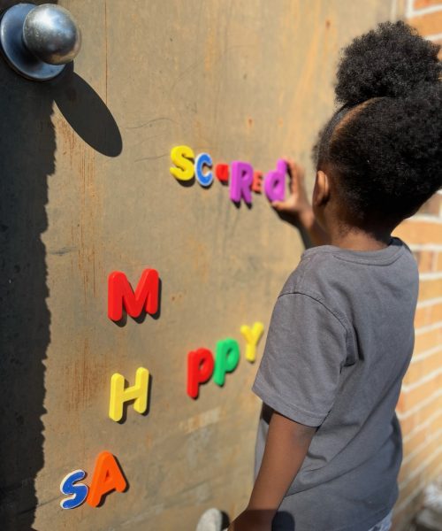 Child arranging colorful magnetic letters on wall.