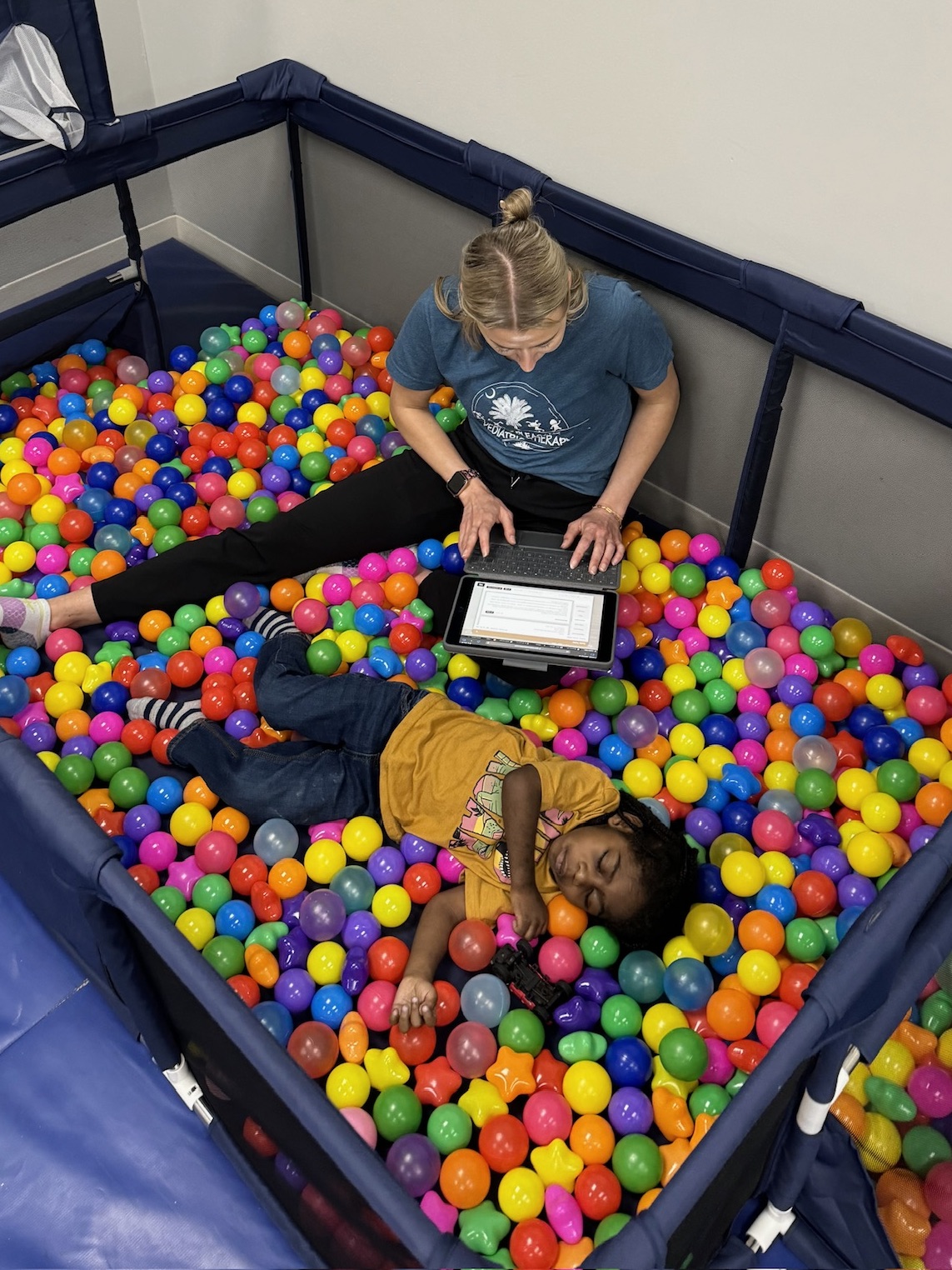 Two kids playing and reading in a colorful ball pit.