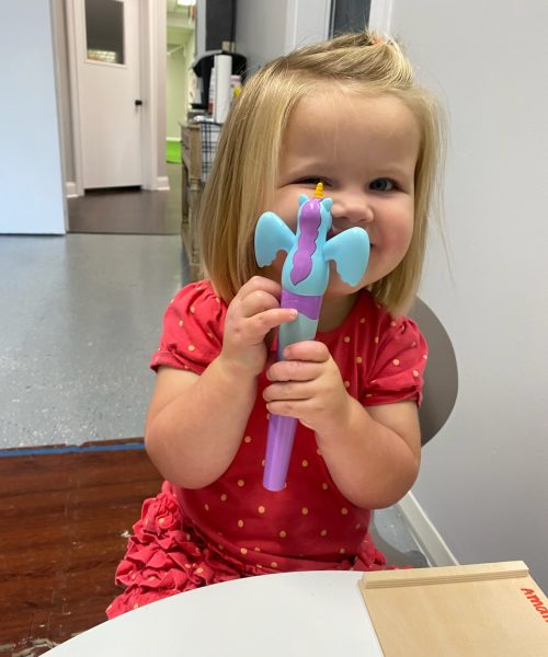 Child smiling, holding a unicorn toy pen.