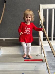 Toddler in red dress on play stairs.