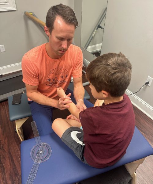 Man examining child's arm on therapy table.