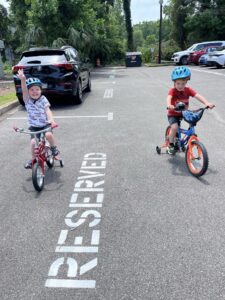 Two kids riding bikes in a reserved parking spot on a sunny day.