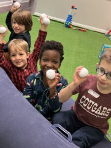 Children happily holding white balls and waving at the camera outdoors.