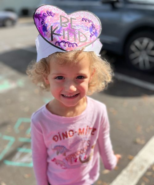 Child wearing "Be Kind" heart-shaped hat.