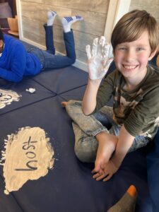 Child smiling with painted hand, sitting indoors.