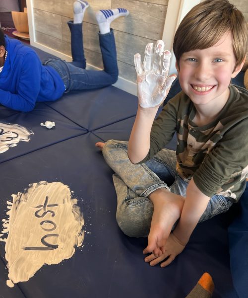 Child smiling, showing painted hand indoors.