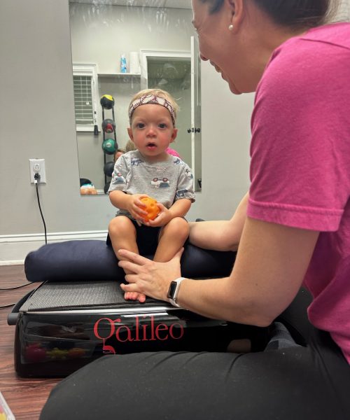 Child sitting with therapist on exercise equipment.