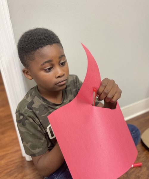 Boy cutting red paper with scissors.