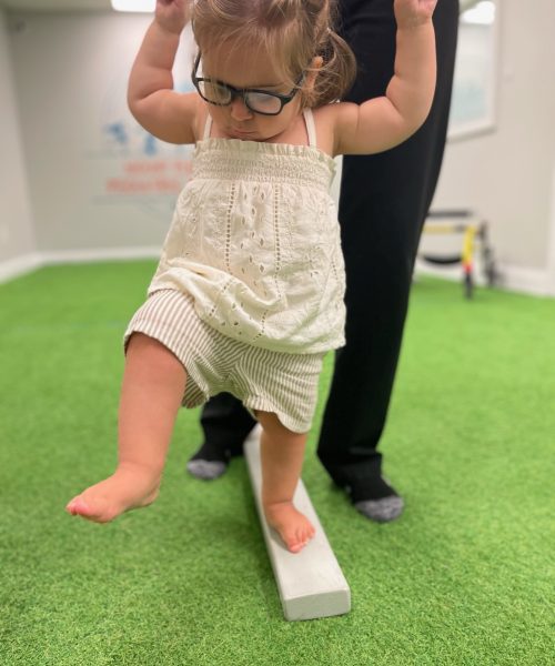 Toddler balancing on beam with assistance.