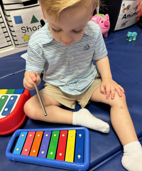 Child playing with colorful xylophone on mat.