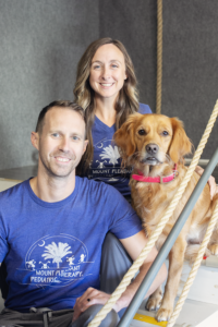 A smiling couple posing with their golden retriever dog indoors.