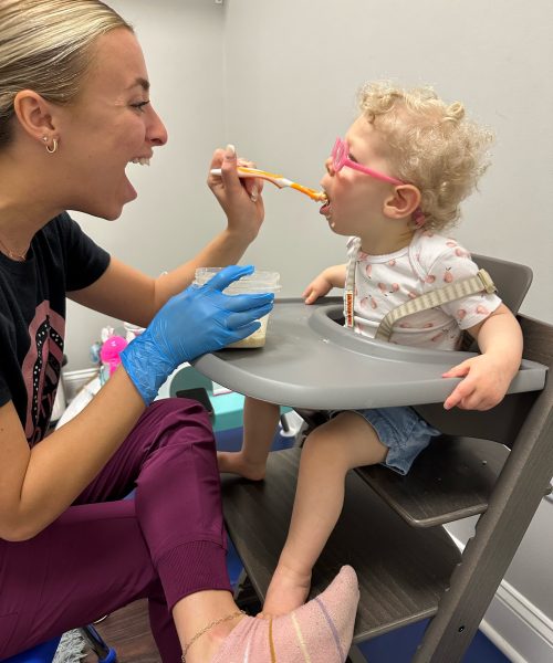 Woman feeding toddler in high chair.