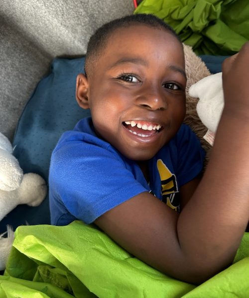Smiling child lying with stuffed animals.