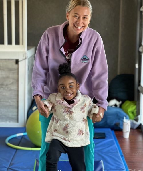 Woman helping child walk on exercise mat.