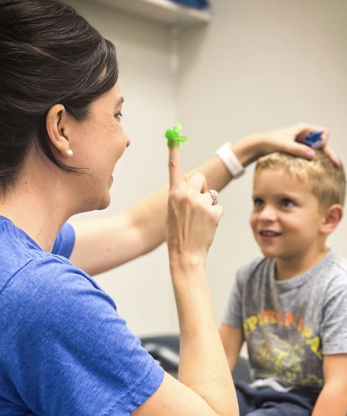 Woman engaging with smiling boy in therapy.
