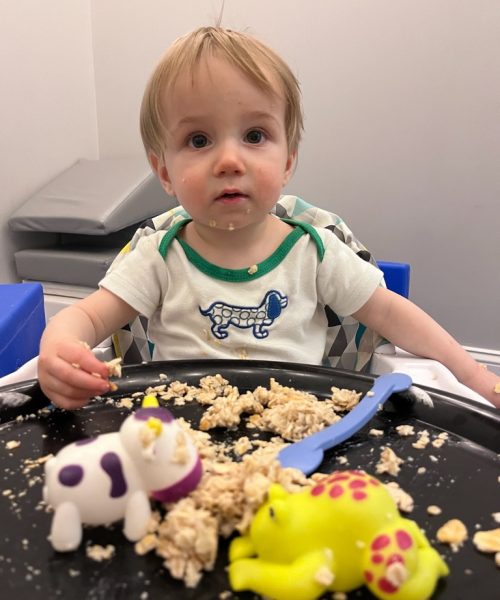 Toddler eating and playing with toys.