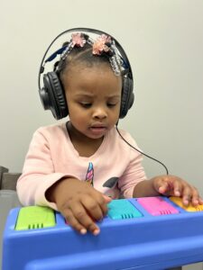 Young girl wearing headphones playing a colorful toy piano.
